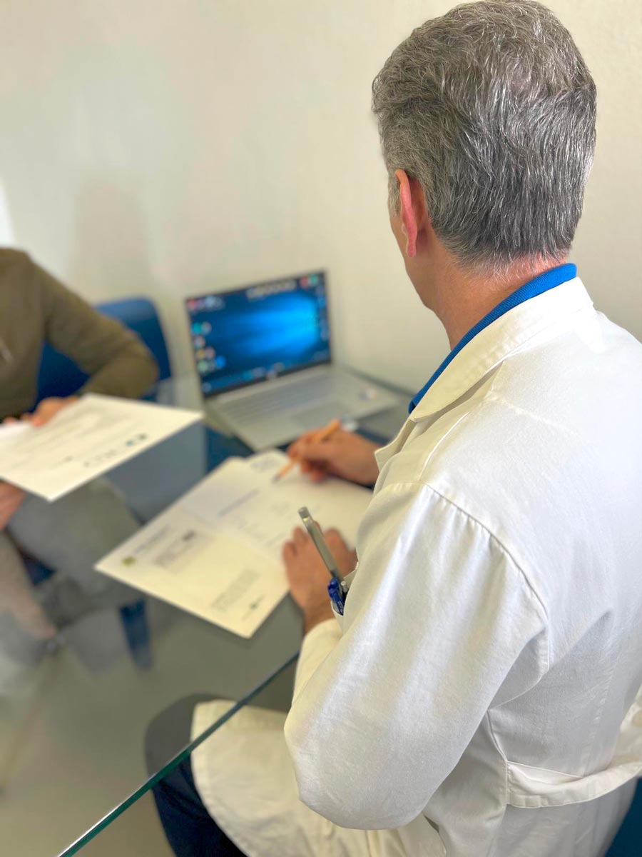 Foto che ritrae un fisiatra al lavoro sul proprio pc con un paziente