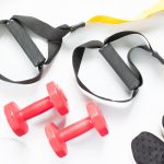 Attrezzatura per allenamento funzionale con manubri, cinghie TRX e scarpe sportive.