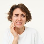 Donna con espressione di dolore che tocca la mascella, segno di possibile disturbo temporo-mandibolare.