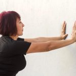 Donna che esegue esercizi di ginnastica posturale appoggiando le mani al muro.