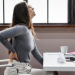 Donna con mal di schiena causato da postura scorretta alla scrivania.