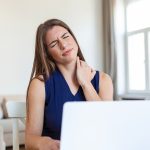 Donna con dolore cervicale mentre lavora al computer, tensione al collo da postura prolungata